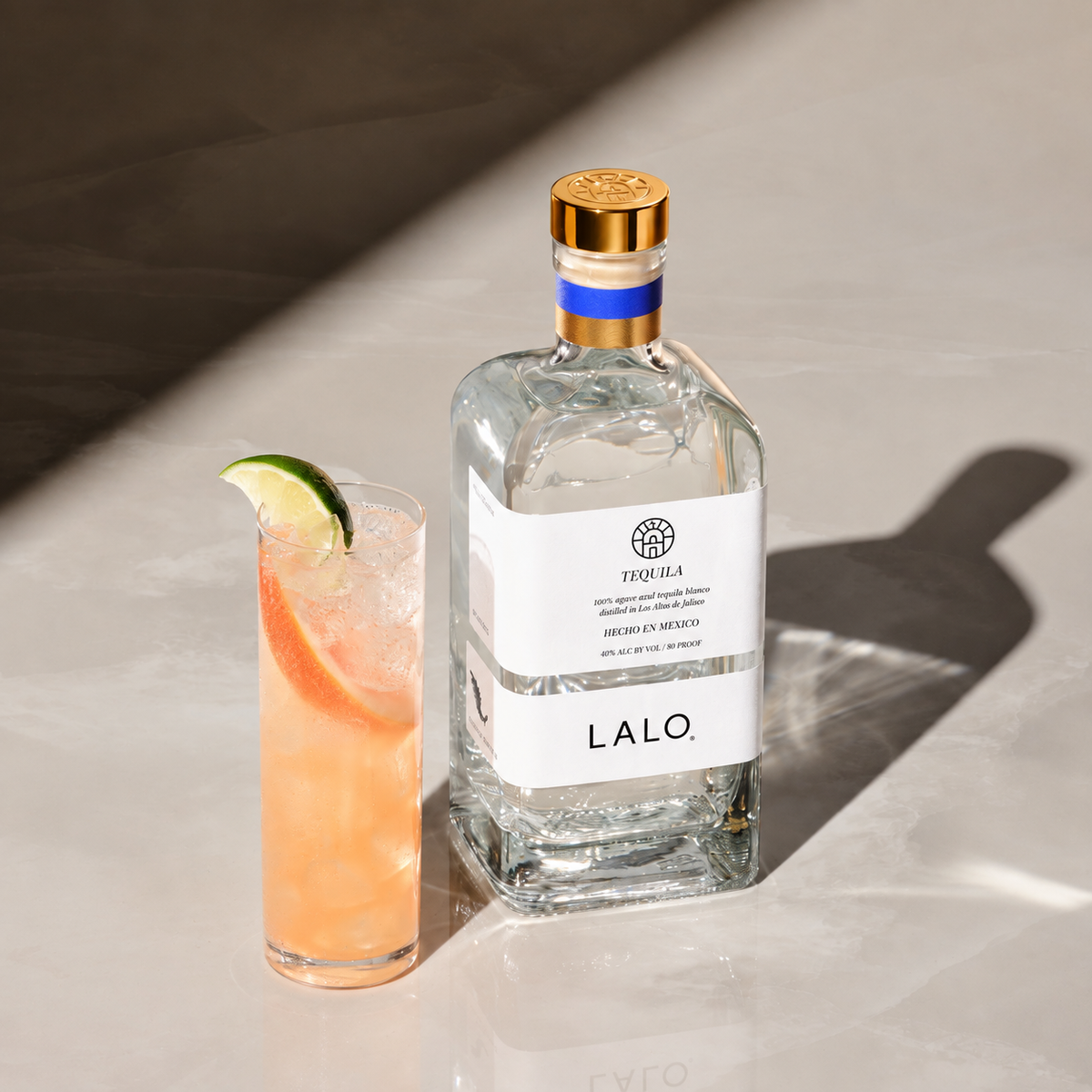 LALO Tequila Blanco bottle beside a pink Paloma cocktail garnished with lime